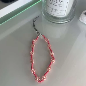 Mobilaccesoar - Egengjord mobilaccesoar med pärlor av olika rosa som utgör en blommdesign. 
