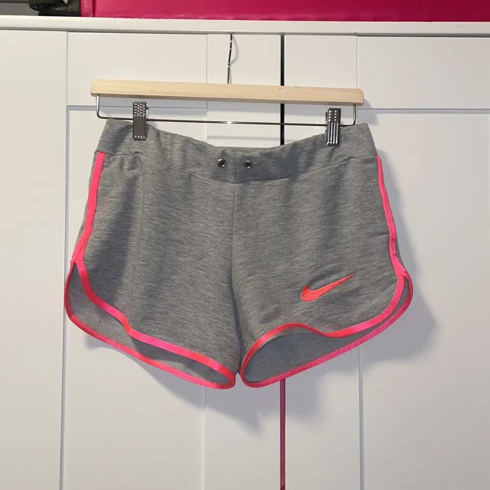 Säljer ett par grå träningsshorts från Nike med snygga rosa detaljer. De har en normal passform och är perfekta för träning eller en avslappnad dag. Shortsen är gjorda i ett mjukt och bekvämt material. Snöret saknas därför säljer jag den billig💕. Accessoarer.