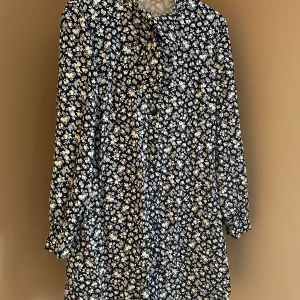 Blommig klänning - Säljer en superfin blommig klänning i mörkblått med vita blommor. Den har långa ärmar och en bekväm passform, perfekt för både vardag och fest. Klänningen är i nyskick med prislapp kvar. Perfekt för att liva upp garderoben!