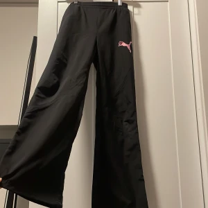 Svarta byxor från Puma - Säljer ett par svarta byxor från Puma med en rosa logga på sidan. Byxorna har en loose passform och är högmidjade med resår i midjan för extra komfort. Perfekta för en avslappnad stil eller träning. Köpt för 399kr säljer för endast 100kr!
