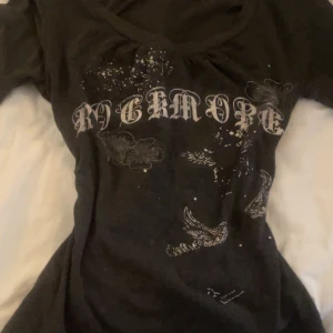 Mörkgrå långärmad topp med tryck - Snygg mörkgrå långärmad topp med tryck i vitt. Toppen har en v-ringad hals och text framtill. Perfekt för en cool och avslappnad stil.