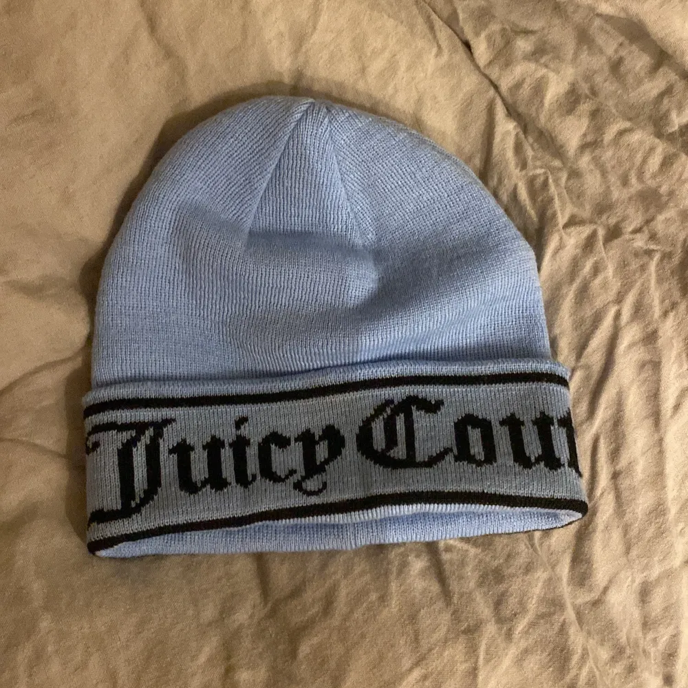 Snygg ljusblå mössa från Juicy Couture med svart textdetalj runt kanten. Perfekt för att hålla sig varm och stilren under kyliga dagar.. Asusteet.
