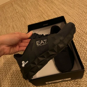 Svarta sneakers från Emporio Armani - Snygga svarta sneakers från Emporio Armani med en unik geometrisk sula och diskret logga på sidan. Skorna har snörning och är perfekta för träning eller vardagsbruk. Storlek 38 2/3. Knappt använda. 