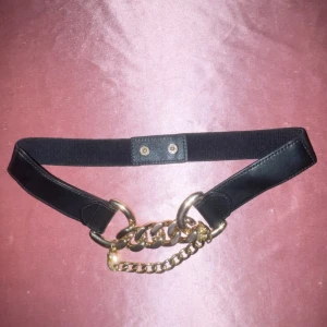 Svart bälte med guldkedja - Snyggt svart bälte med en iögonfallande guldkedja framtill. Bältet har en elastisk del och knäpps med tryckknappar. Perfekt för att ge en extra touch till din outfit.