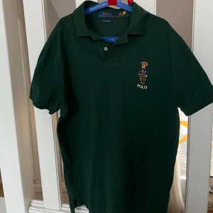Grön pikétröja från Polo Ralph Lauren - Ny, aldrig använd. Säljer en klassisk grön pikétröja från Polo Ralph Lauren. Tröjan har korta ärmar och en traditionell krage med knappar. Perfekt för en stilren look.