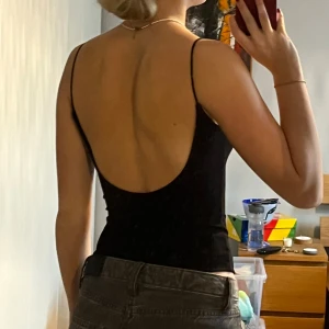 Svart ribbad body  - Snygg svart ribbad body med smala axelband och öppen rygg. Perfekt för en stilren look. Sitter lagom tajt mot brösten för ett mjukt stöd.