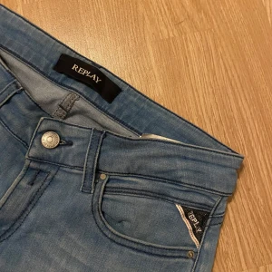Blå jeans från Replay - Snygga blå jeans från Replay med klassisk femficksdesign och knappgylf. Perfekta för en avslappnad stil. Märkesdetaljer på bakfickan och bältesslingan.Storlek 28:32👊🏻