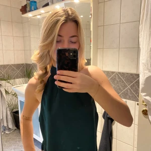 Mörkgrön ärmlös festtopp - Snygg mörkgrön topp med öppen rygg och halterneck-design. Perfekt för fest