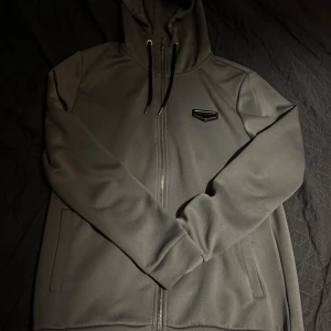 Grå huvtröja från Supply & Demand - Snygg grå huvtröja från Supply & Demand med dragkedja och justerbar huva. Är både perfekt och varm för en avslappnad stil. Tröjan har långa ärmar och en diskret logga på bröstet.