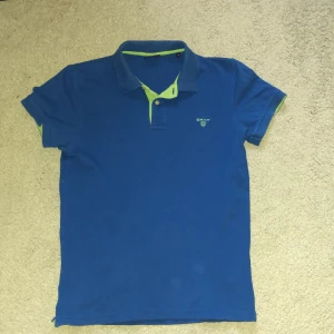 Gant pike - Snygg blå pikétröja från GANT med gröna detaljer och en klassisk krage. Perfekt för en avslappnad stil. Kortärmad design med en liten logotyp på bröstet.