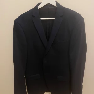 Mörkblå kavaj från Tiger of Sweden - Snygg mörkblå kavaj från Tiger of Sweden strl 48. Klassisk design med två knappar framtill och fickor. Perfekt för både formella och semi-formella tillfällen. Stilren och tidlös. Använd fåtal gånger, inga skavanker. 