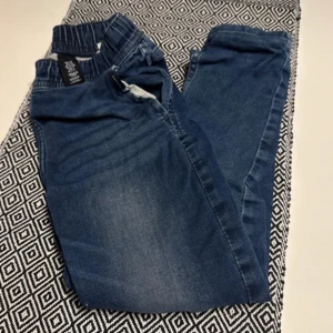 Blå jeansbyxor med resårmidja - Säljer ett par bekväma blå jeansbyxor med resårmidja. Perfekta för en avslappnad stil. De har en klassisk blå färg och är gjorda i ett mjukt material för extra komfort.