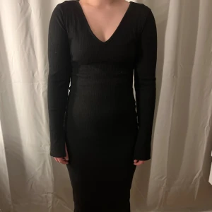 Svart ribbad klänning från lager157 - Snygg svart ribbad klänning från lager157 i storlek S. Klänningen har en v-ringad hals och långa ärmar med en slit. Materialet består av polyester, viskos och elastan.