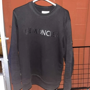 Svart sweatshirt från Moncler - Snygg svart sweatshirt från Moncler med logotyp tryckt på bröstet och ett märke på ärmen. Perfekt för en stilren och avslappnad look. Tröjan har långa ärmar och rund halsringning.