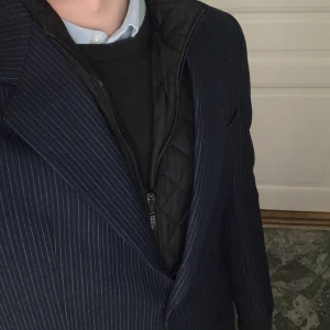 Mörkblå randig kavaj från Tiger of Sweden - Snygg mörkblå kavaj med  ränder från Tiger of Sweden. Kavajen har klassiska slag och två knappar framtill. Perfekt för en stilren look. Storlek 52 och är i 100% ull, och passar därför perfekt till kallare årstider. Priset är inte hugget i sten 🪨 