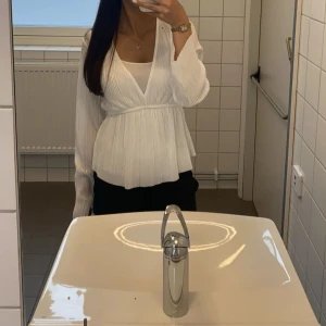 Vit blus med v-ringning - Elegant vit blus med v-ringning och långa ärmar. Blusen har en omlott-design och är lätt ribbad, vilket ger en stilren look. Perfekt för både vardag och speciella tillfällen. Sen är ganska genomskinlig men då kan man göra som jag o nära ett tunt linne under🫶🏻🫶🏻skriv för fler bilder, ja svarar fort