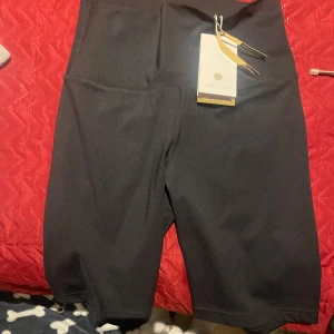 Svarta cykelshorts från Athleta - Säljer ett par svarta cykelshorts från Athleta. De är högmidjade och perfekta för träning. Materialet är stretchigt och bekvämt, vilket gör dem idealiska för intensiva pass. Passformen är tight och de har en stilren design utan onödiga detaljer.