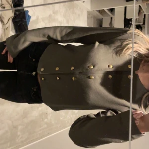 Olivgrön kofta med guldknappar - Säljer en super fln olivgrön kofta med snygga guldknappar. Koftan har långa ärmar och en klassisk passform som passar perfekt till både vardag och mer uppklädda tillfällen.