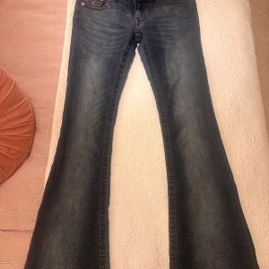Blå jeans från True Religion - Säljer ett par snygga blå jeans från True Religion med låg midja och bootcut-stil. De har coola röda sömmar och en unik tvätt för en sliten look. 