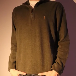 Olivgrön tröja från Polo Ralph Lauren - Säljer en stilren olivgrön tröja från Polo Ralph Lauren med dragkedja vid halsen. Tröjan har långa ärmar och är tillverkad i ett mjukt material som passar perfekt för kyligare dagar.