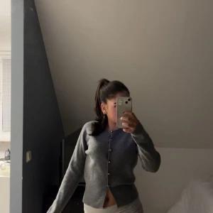 Grå kofta med knappar - Säljer en stilren grå kofta med knappar framtill. Koftan har en klassisk design med rund hals och långa ärmar. Koftan är i mycket bra skick🫶🏽