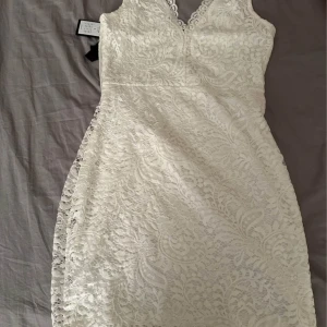 Vit spetsklänning från Vero Moda - Oanvänd då den va för stor för mig. En elegant vit spetsklänning från Vero Moda med v-ringad hals och ärmlös design. Perfekt för sommarens festligheter med sin fina spetsdetalj och figurnära passform.