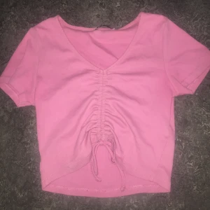 Rosa crop top med knyt - Säljer en söt rosa crop top med v-ringning och knytning framtill✨ Toppen är kortärmad och croppad, perfekt för en avslappnad stil.😍