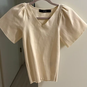 Beige topp  - Snygg beige topp från Vero Moda med korta ärmar och v-ringning. Toppen har en figurnära passform och är använd 2 gånger💕