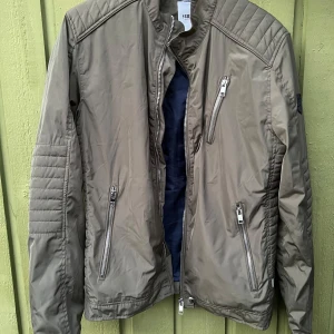 Olivgrön jacka från Solid - Snygg olivgrön jacka från Solid med dragkedjor och quiltade detaljer på axlarna. Jackan har flera praktiska fickor med dragkedja och en stilren design som passar perfekt för höst och vår.