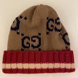 mössa från Gucci - Snygg stickad mössa från Gucci. Mössan har ett ikoniskt GG-mönster i mörkblått och är tillverkad i Italien. Perfekt för att hålla sig varm med stil. Mössan är självklart äkta.