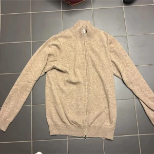 Beige kashmirtröja från Davida - Säljer en mjuk och stilren beige kashmirtröja från Davida. Tröjan har en dragkedja framtill och långa ärmar. Perfekt för kyliga dagar och ger en lyxig känsla. Passar bra till både jeans och kjol. Tröjan har 4 defekter på sig, men de syns knappt. Köptes i vintras, nypris 2800kr