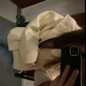Beige kappa från Noisy May - Säljer en vit skit snygg kappa från Vero Moda. Jackan är kortare med stora knappar och bred krage. Perfekt för lite festligare tillfällen. Passar bra till både jeans och klänning.