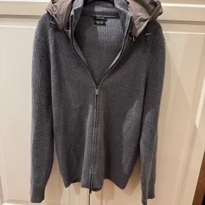 Grå Massimo Dutti - Snygg grå stickad cardigan från Massimo Dutti med dragkedja och avtagbar huva. Perfekt för kyliga dagar med sin ribbade design och långa ärmar. En stilren och praktisk tröja för alla tillfällen.