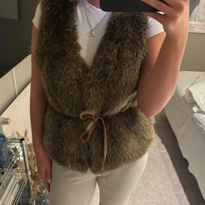 Brun pälsväst med knytband - Säljer en mysig brun pälsväst med knytband i midjan. 