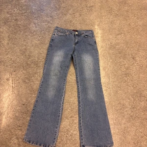 Blå jeans från Nina Rossi - Snygga blå jeans från Nina Rossi med broderade detaljer på bakfickorna. De har en klassisk bootcut-stil och är perfekta för en avslappnad look. Jeansen har en knapp och dragkedja framtill.