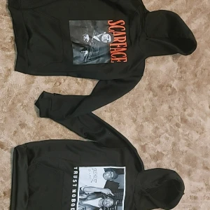 Svarta hoodies med Scarface och Tupac motiv - Två svarta hoodies med tryck. Ena har Scarface-motiv med texten 'Say Good Night to the Bad Guy' i rött. Den andra har Tupac-motiv med texten 'Trust Nobody'. Perfekta för streetwear-stilen. 200 kr styck