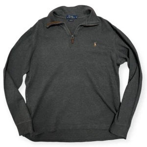Grå half zip tröja från Ralph Lauren - Säljer en stilren grå tröja från Polo Ralph Lauren med halv dragkedja och broderad logotyp på bröstet. Perfekt för en avslappnad men snygg look. Tröjan har långa ärmar och en bekväm passform. Ställ frågor om du undrar något om tröjan eller priset!
