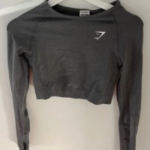 Grå croppad tröja från Gymshark - Säljer en grå croppad tröja från Gymshark. Tröjan har långa ärmar och en tight passform, perfekt för träning. Den är tillverkad i ett syntetmaterial som andas bra. Helt ny.