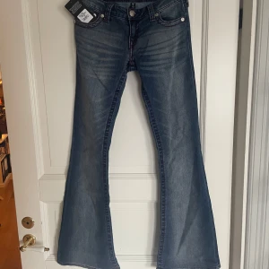 Blå jeans från True Religion - Snygga blå jeans från True Religion med en flare-stil och låg midja. De har dekorativa sömmar och knappar med märkets logga. Säljer jeansen så de är lite för korta för mig som är 170cm. Hör av dig för fler bilder🥰