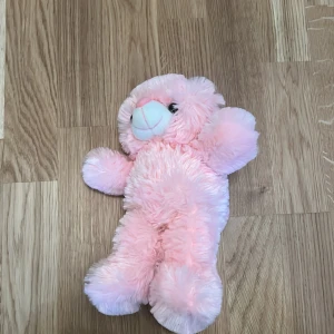 Rosa nallebjörn - Mjuk och fluffig rosa nallebjörn med vita detaljer på nosen. Perfekt som kramkompis eller dekoration i barnrummet. Den har en söt och vänlig design som passar alla åldrar.