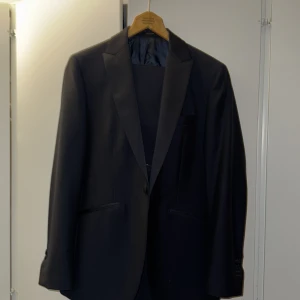 Svart kostym från Massimo Dutti - Elegant svart kostym från Massimo Dutti. Kavajen har en klassisk design med knappar och byxorna är stilrena från märket Tiger of Sweden. Perfekt för formella tillfällen. 