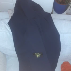Blå softshell-jacka från Stone Island - Säljer en Mörkblå softshell-jacka från Stone Island i bra skick. Jackan har en stilren design med det klassiska Stone Island-märket på ärmen. Perfekt för höst och vår med sitt vattenavvisande material och bekväma passform. Dragkedja framtill och flera praktiska fickor. Passar både till vardags och lite finare tillfällen.