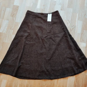 Brun kjol från Rihoas - Säljer en snygg brun kjol från Rihoas i nytt skick. Kjolen har en klassisk A-linjeform som passar perfekt för både vardag och fest. Materialet känns robust och av hög kvalitet. Den är enkel att matcha med olika toppar och accessoarer. Perfekt för höst och vinter!