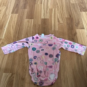 Rosa blommig body från Parvel - Söt rosa body med blommigt mönster i flera färger från Parvel. Den har långa ärmar och praktiska tryckknappar vid axeln och grenen. Perfekt för de minsta! 🌸