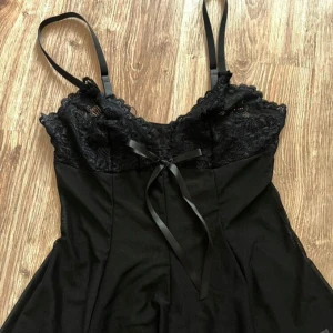 Svart Spetsnattlinne med rosett  - Spetsnattlinne med smala axelband. Storlek S. Går att chystera i axelbanden. Längd 19cm. Midja storlek 64-90 cm. Underbyst/ byst 60-70cm ORDINARIE PRIS 200kr Säljer för 120kr. Oanvänd. Märke Nelly.
