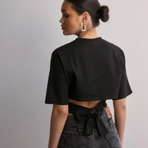 Svart croppad topp med knyt - Snygg svart croppad topp med knyt i ryggen. Toppen har korta ärmar och en stilren design som passar perfekt till både jeans och kjol. Perfekt för en trendig look!