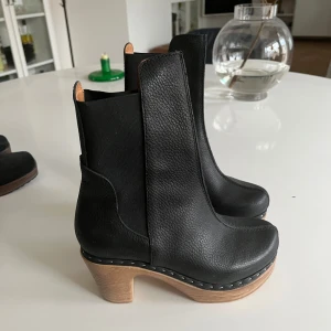 Svarta boots med träklack - Snygga svarta boots i skinn från Calou Stockholm. Helt nya och oanvända. Nypris 2900kr. Mjuk, lätt och böjbar sula. Storlek 37, normal i storleken.