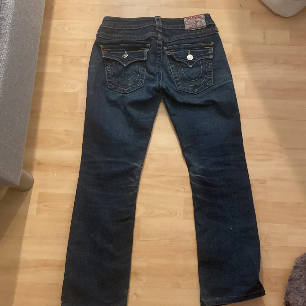 Snygga mörkblå jeans från True Religion med ikoniska bakfickor och kontrastsömmar. Jeansen har en klassisk femficksdesign och knappgylf. Perfekta för en avslappnad stil. De har ett hål vid låret men de är inget man ser på, jag har även sytt på hålen med de e fortfarande ett hål( Skriv för bilder) orginalprid 2296kr. Farkut & Housut.