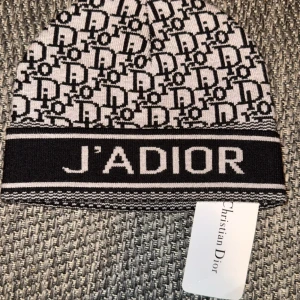 Svartvit mössa från Christian Dior - Snygg svartvit mössa från Christian Dior med texten 'J'ADIOR' och ett elegant mönster. Perfekt för att hålla stilen i kallare väder.