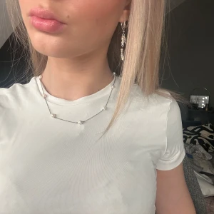 Silverhalsband med pärlor - Säljer ett elegant silverhalsband med små vita pärlor. Perfekt för att ge en touch av klass till vilken outfit som helst. Halsbandet är enkelt men stilrent och passar både till vardags och fest. Det har en justerbar kedja för att passa olika längder.
